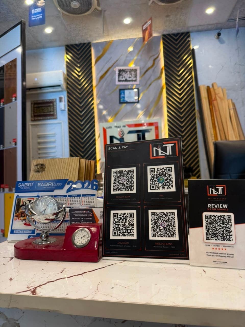 A payment QR card and a Google review card by TapCard standing on the counter at Muzafar & Sons, Lucky Traders